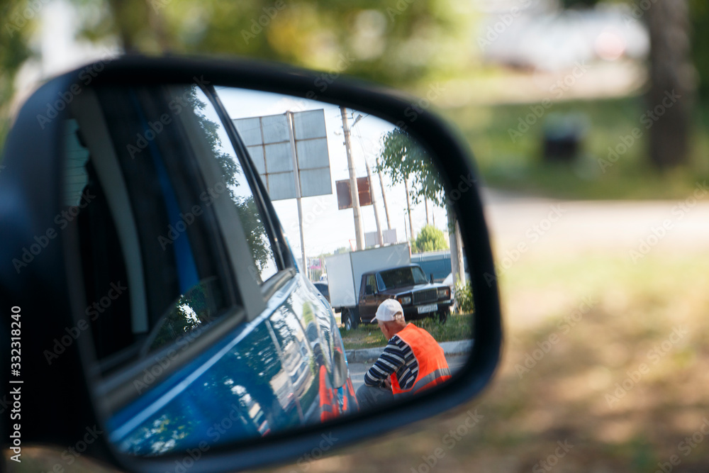 reflection of a street cleaning worker in the rearview mirror of a car