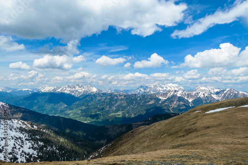 A vast view on Alpine valley from the upper parts of Himmeleck in Austria. The valley is lush green. There are many mountain ranges in the back, covered with snow. Spring coming to the Alps. photo