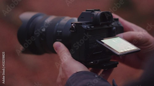 Guy photographer using a mirrorless camera with a screen to make a video of photo in a forest on a early morning with a Sony A7III photo