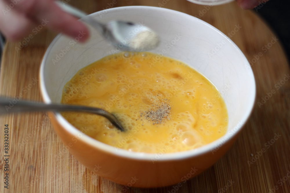 Fotografie Adding white ground pepper into beaten eggs in bowl