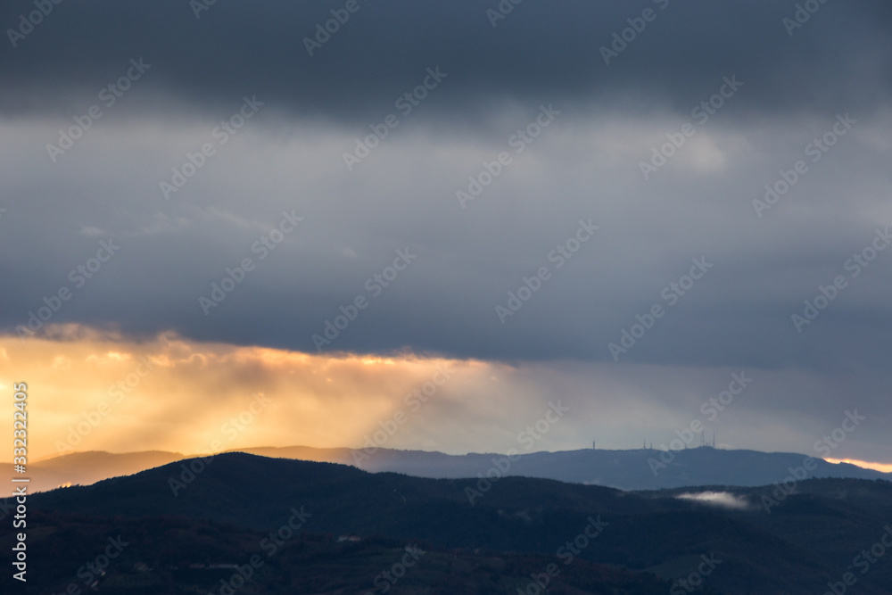 Sunrays coming over mountains beneath moody clouds