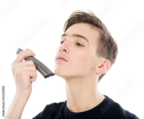 Teenage boy is shaving at first time his mustaches with an electric razor. Young man shaves his face with a electric razor