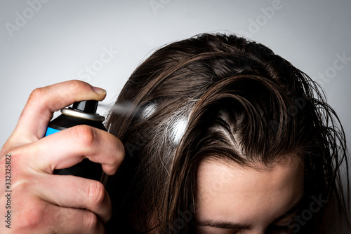 Woman applying dry spray shampoo on her dirty hair. Fast and easy way to keep your hair clean. photo