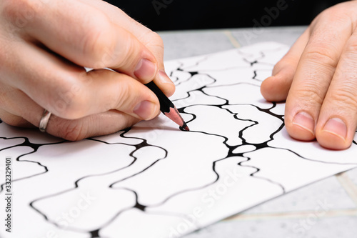 Man is drawing an abstract imaginary picture of curves by a black pencil in his hand. A psychological art therapy tests. Identification of the unconscious, subconscious, the depths of the human brain.
