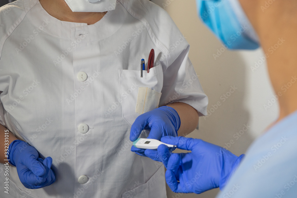 Nurse gives thermometer to another nurse. Nurses wear blue gloves and face masks. High fevers are symptoms of the coronavirus. Nurse gives thermometer to another nurse. Nurses wear blue gloves and face masks. High fevers are symptoms of the coronavirus.