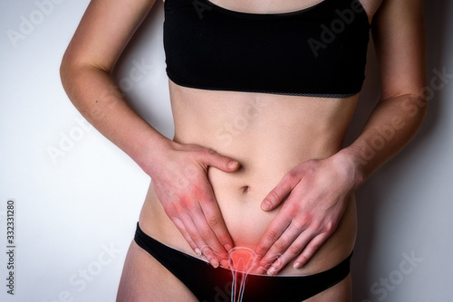 Woman suffering from stomach pain. Young woman with hands holding her crotch lower abdomen gray background.