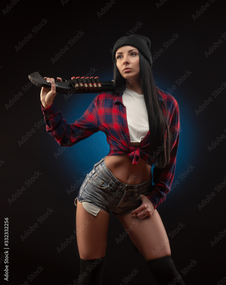 Fototapeta premium the girl in a checked shirt on a dark background with a shotgun