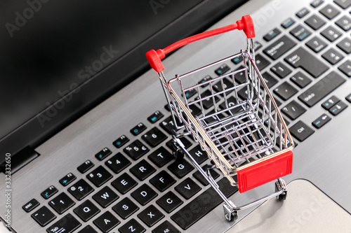 Laptop keyboard with a toy shopping cart standing on it. Close up. Top view. Copy space. Concept of online shopping and modern technologies
