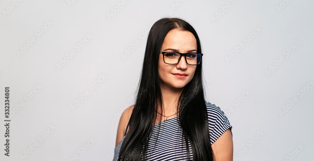 Young girl in glasses dressed in a grey T-shirt stands on a white background. Presenting glasses. Young girl in glasses dressed in a grey T-shirt stands on a white background. Presenting glasses.