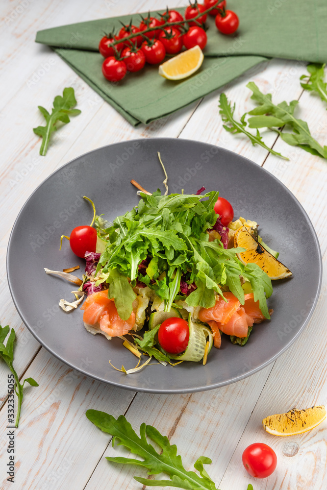 Healthy salmon mix salad with sesame-honey dressing, slices of fish, cherry tomatoes, arugula and pickled cucumber, lunch menu of national food restaurant on white wooden background in rustic style Healthy salmon mix salad with sesame-honey dressing, slices of fish, cherry tomatoes, arugula and pickled cucumber, lunch menu of national food restaurant on white wooden background in rustic style