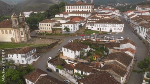 Aerial descend over the rooftops of Ouro Preto, Minas Gerais, Brazil, city centre with typical colonial architecture with market and Assissi church in the background panning towards street level photo