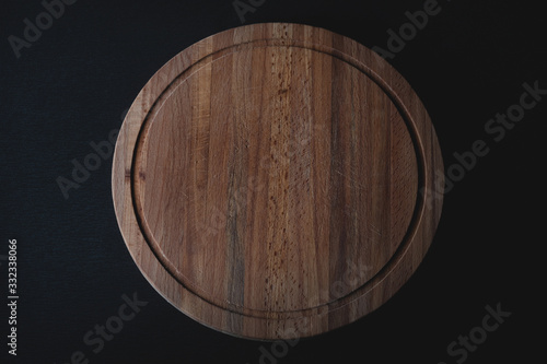Wooden round cutting board on a black background. Empty board close up. Object is highlighted.