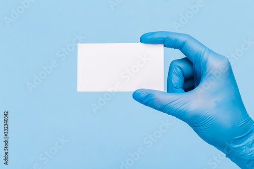 female hand in a medical glove holds a blank form of paper on a blue background. Mock up, business card