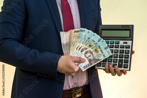 businessman in suit hold calculator and lot of ukraine money, UAH, grivnya, isolated photo