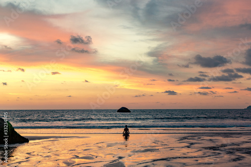 young unrecognizable woman meditating at agonda beach at sunset in goa, india