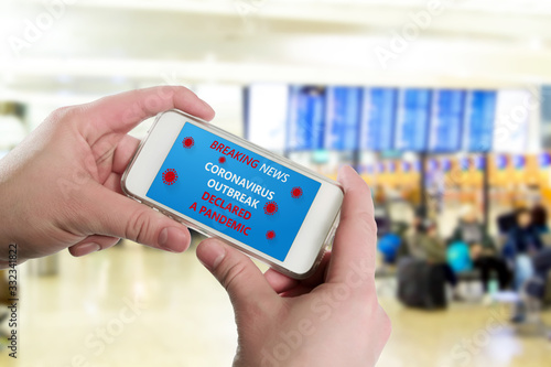 hand holds smartphone with announcement of Breaking news, Coronavirus outbreak declared pandemic in background of waiting room at airport. Concept of the spread of new coronavirus disease COVID-19.