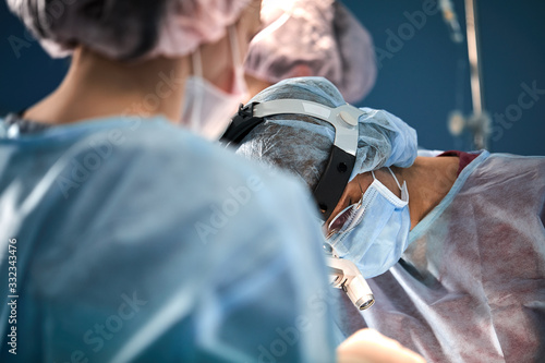 Surgical team in the operating room, close-up. An international team of professional doctors in a modern operating room is undergoing surgery. Saving lives, modern medicine, blue blue light