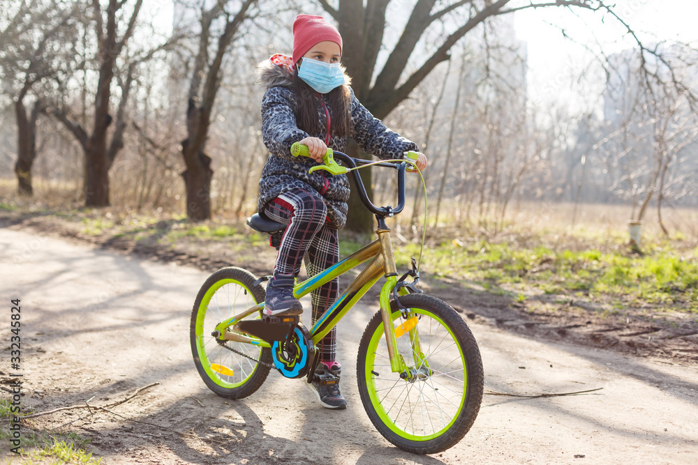 Little girl wearing medical mask prevent flu, pollutions and covid-19 riding bicycle outdoor.