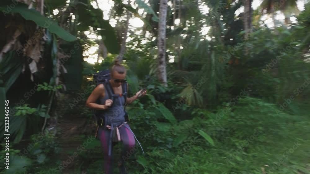 A white Caucasian girl with a large backpack is walking along a trail in tropical terrain. Jungle. Travels in Asia. A tropical forest. Tourist. Hiking. Campaign. Forest area. A white Caucasian girl with a large backpack is walking along a trail in tropical terrain. Jungle. Travels in Asia. A tropical forest. Tourist. Hiking. Campaign. Forest area.