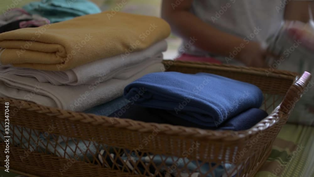 Woman is folding clothes and putting into a wooden basket. Housewife doing some house work in bedroom. Close up a pile of folded clothes on the bed.