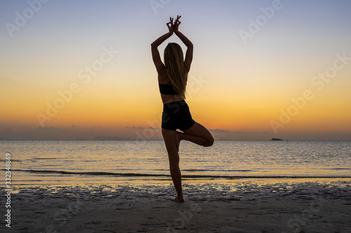 Silhouette of woman standing at yoga pose on the tropical beach during sunset. Girl practicing yoga near sea water © OlegD