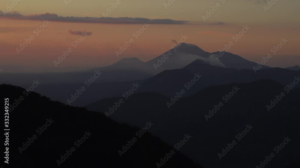 Zoom out timelapse of Telica and San Cristóbal volcano, in Nicaragua, smoking in the distance behind layers of hills and mountains during sunset. Zoom out timelapse of Telica and San Cristóbal volcano, in Nicaragua, smoking in the distance behind layers of hills and mountains during sunset.