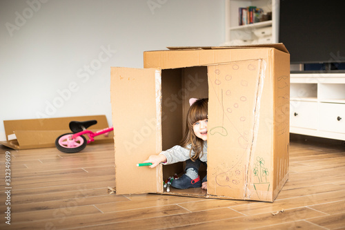 Caucasian little child looking out of a cardboard playhouse. Material recycle, eco friendly, sustainability concept, simple fun idea for entertaining children at home. photo