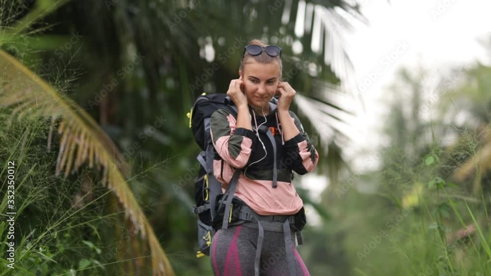 A young charming girl with a large tourist backpack listens to music on headphones. A young charming girl with a large tourist backpack listens to music on headphones.