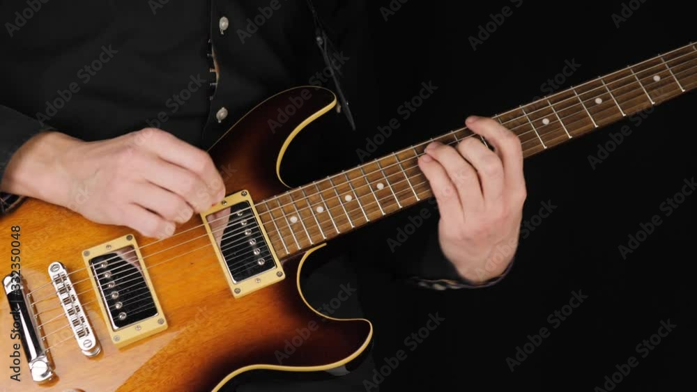 Guitarist plays a light brown six-string electric guitar with a pick against black background. Concept of stay at home and make some music. Free time for sound art. Wide shot. 4K Guitarist plays a light brown six-string electric guitar with a pick against black background. Concept of stay at home and make some music. Free time for sound art. Wide shot. 4K