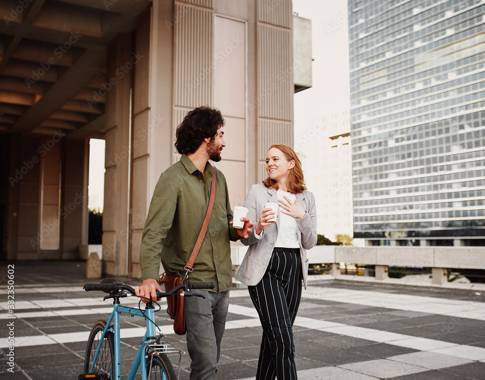 Businessman with cycle and sling bag walking with woman holding disposable coffee cup Businessman with cycle and sling bag walking with woman holding disposable coffee cup
