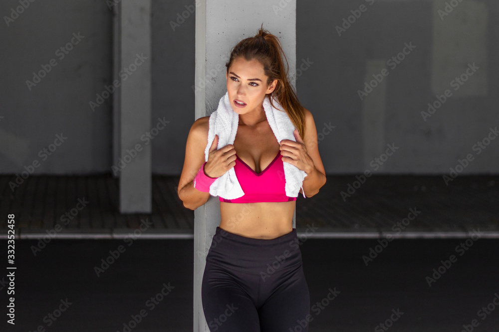 Portrait of adorable charming smiling young shape fitness girl with earphones holding a towel and posing. Fitness woman taking a break after running workout.