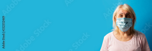 Old woman in protective medical mask on a blue isolated background. The concept of coronavirus, pandemic, no virus, stop, individual protection. Banner. copy space