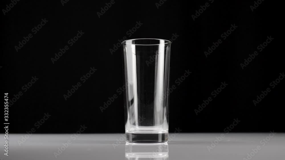 Ice cubes fall into a transparent glass against black background. Concept of stay at home and eat healthy food with natural water. Wide shot. Slow motion Ice cubes fall into a transparent glass against black background. Concept of stay at home and eat healthy food with natural water. Wide shot. Slow motion