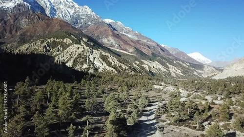 A path through a forest in Manang Valley in Nepalese Himalayas. Sharp and barren peaks of Annapurna chain in the back. Annapurna Circuit Trek. Beauty of the nature. Dusty road.