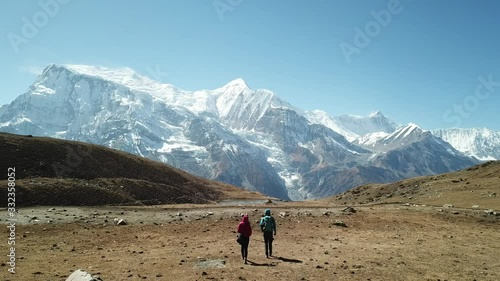 Couple trekking to Ice lake, part of the Annapurna Circuit Trek, Himalayas, Nepal. They are happy. Annapurna chain in the back, covered with snow. Clear weather, dry grass, snowy peaks. High altitude