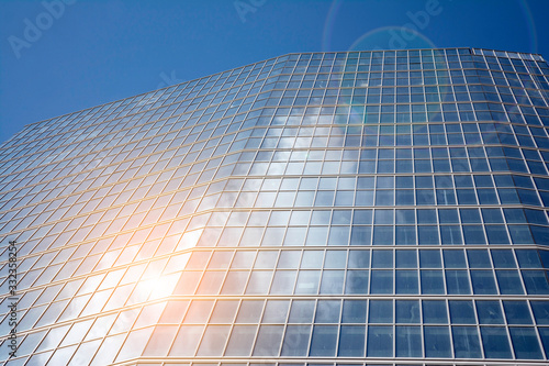 Office building glass facades on a bright sunny day with sunbeams in the blue sky. Abstract view of a skyscraper with sunlight