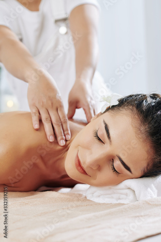 Smiling pretty young woman enjoying shoulder massage in spa salon