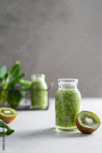 Fresh organic green smoothie with spinach, apple and kiwi in a glass bottle on light background. Detox menu, dieting, healthy food. Side view, copy space