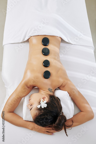 Beautiful slim woman resting on bed in spa salon with hot stones on her spine, view from above