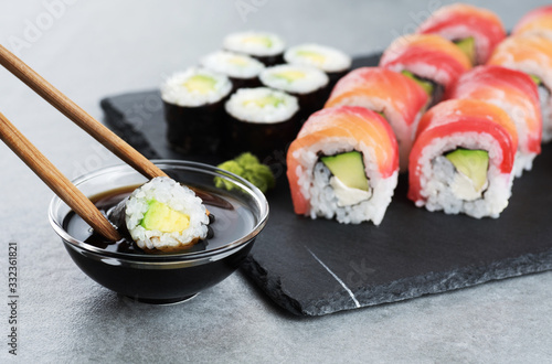 Sushi maki with avocado, sushi philadelphia, soy sauce and wasabi. Chopsticks taking portion of sushi roll.