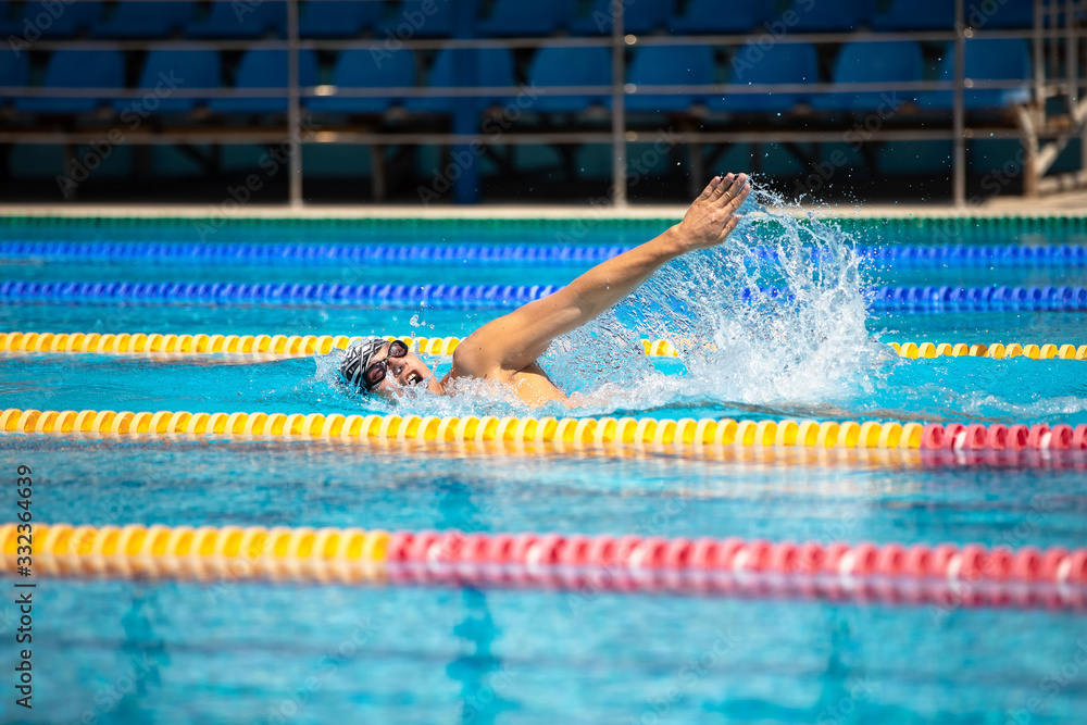 Athletic man swimming in front crawl style in the swimming pool with clear blue water.
