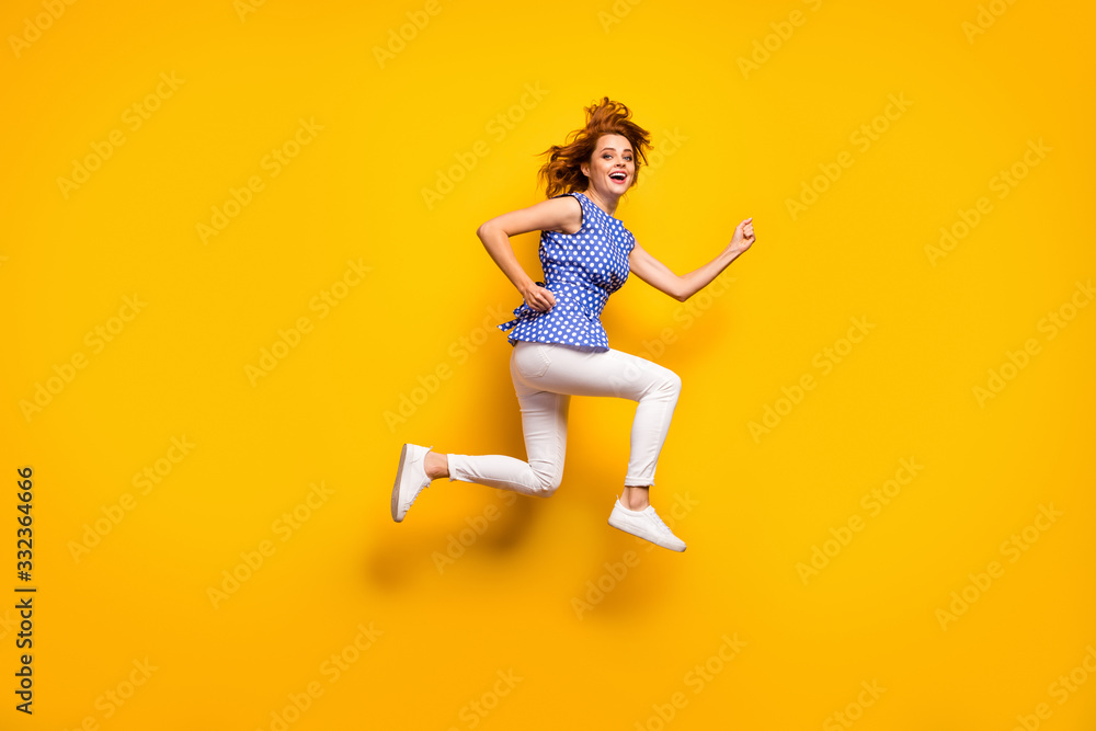 Full body photo of pretty crazy lady jumping high up rushing shopping center black friday shopper wear dotted blue shirt white trousers shoes isolated yellow color background Full body photo of pretty crazy lady jumping high up rushing shopping center black friday shopper wear dotted blue shirt white trousers shoes isolated yellow color background