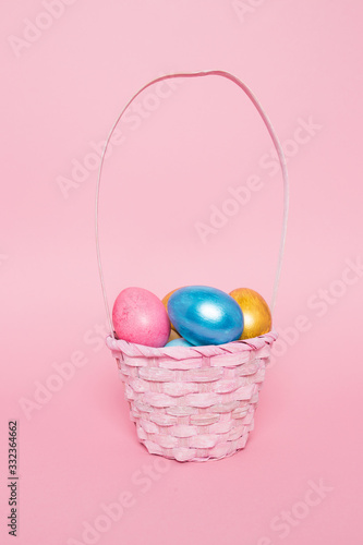 Multi-colored Easter eggs in a basket on a pink isolated background. Easter is a bright holiday.