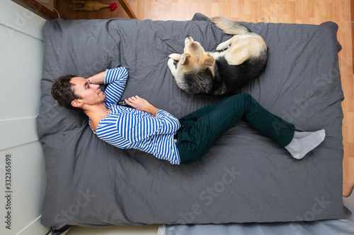 Man and dog lying on bed with gray sheet