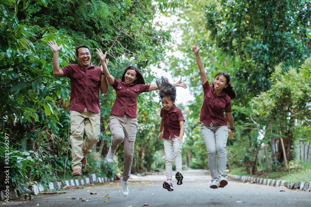 Obraz premium Happy family jumping with raised hands in park during daytime