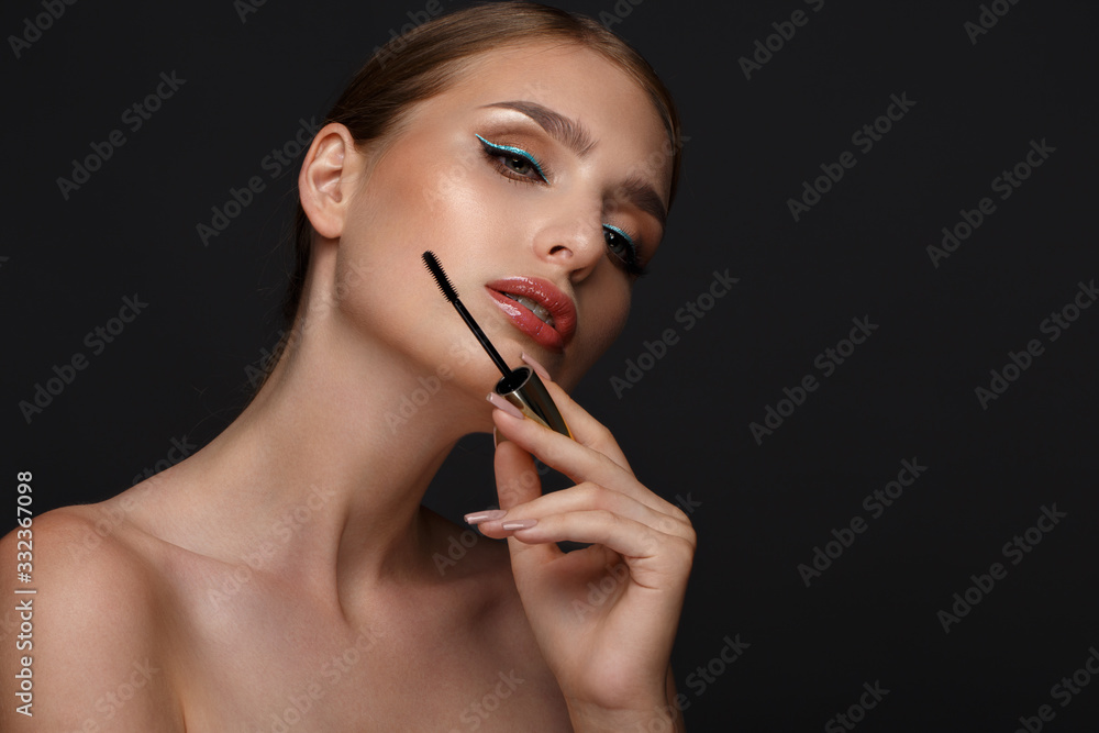 Obraz premium Beautiful girl with sexy lips and classic makeup with cosmetic mascara brush in hand. Beauty face.