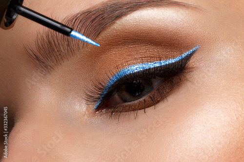 Beautiful girl with sexy lips and classic makeup with cosmetic blue eyeliner in hand. Beauty face. photo