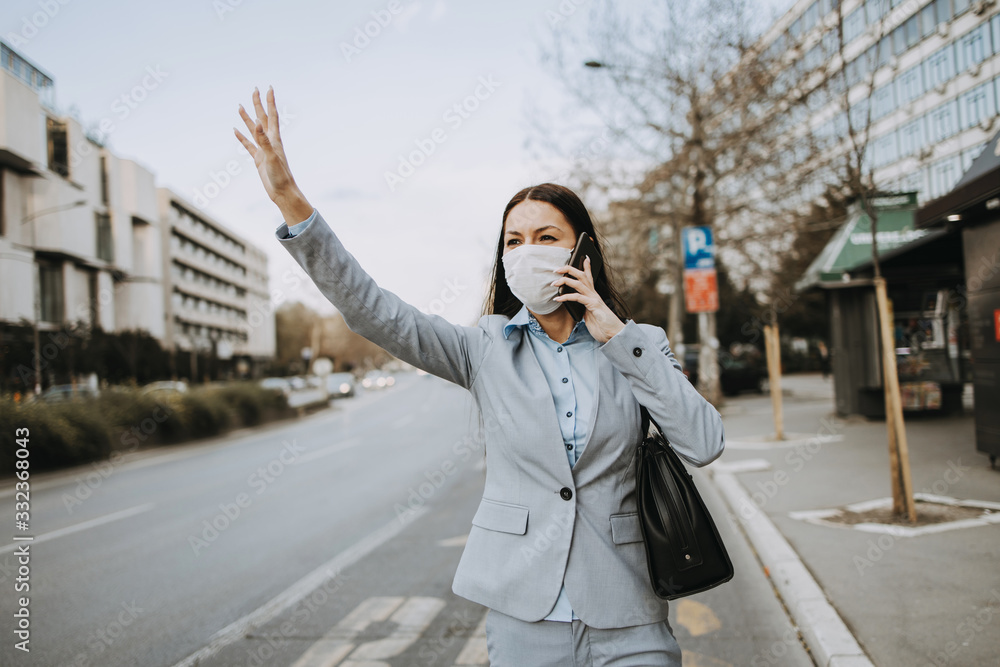 Elegant business woman with protective mask standing alone on empty street and calling for bus or taxi transport with raised hand. Corona virus or Covid-19 lifestyle concept. Elegant business woman with protective mask standing alone on empty street and calling for bus or taxi transport with raised hand. Corona virus or Covid-19 lifestyle concept.
