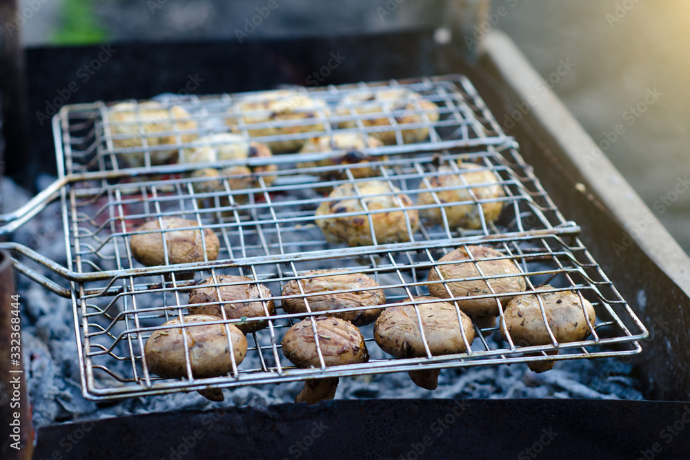 Delicious champignon mushrooms in soy sauce and mayonnaise are fried in grid on grill steam, on homemade grill, closeup