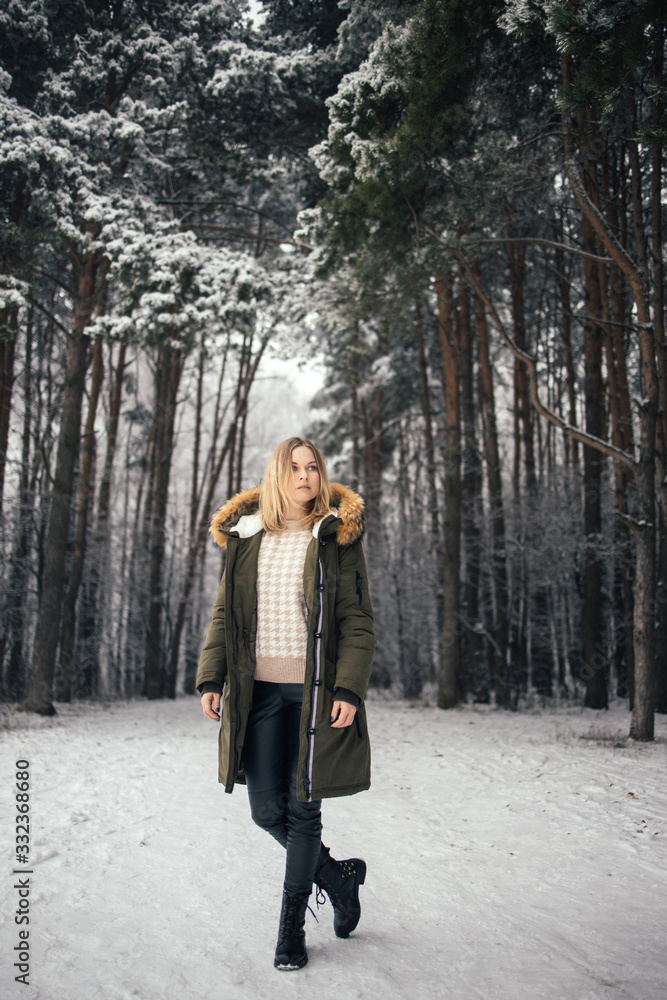 Young woman in full growth on background of snowy trees on walk in winter forest